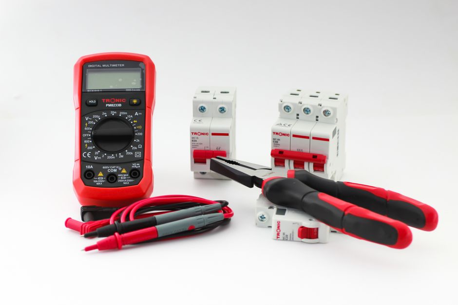 Close-up of a digital multimeter with electrical tools and circuit breakers on a white background.